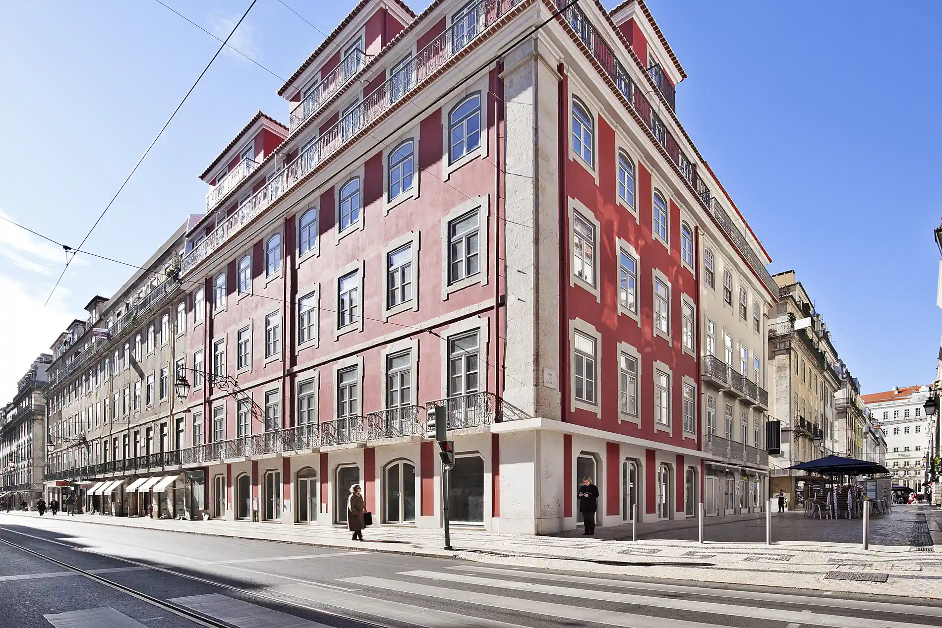 Edif&iacute;cio vermelho cl&aacute;ssico em esquina urbana com c&eacute;u azul ao fundo.