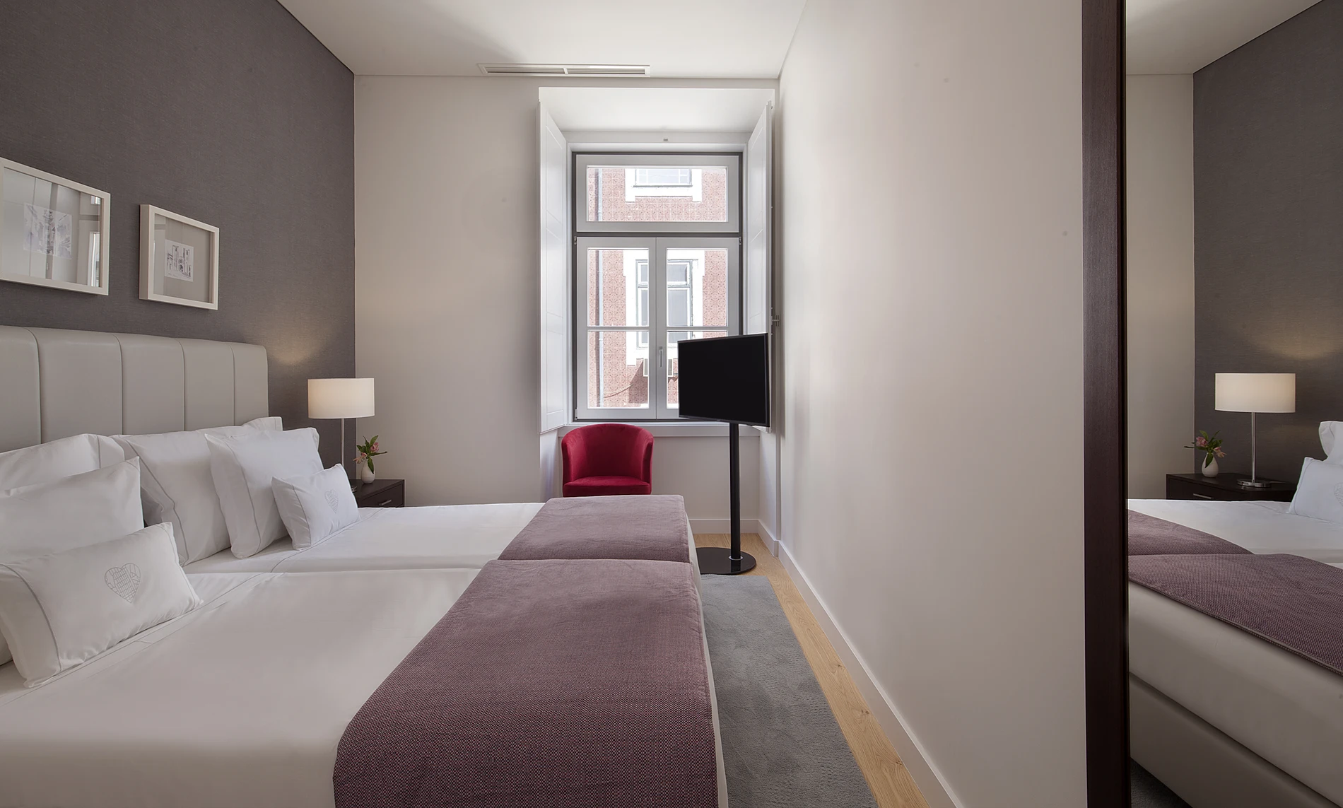 Quarto de hotel moderno com camas duplas, poltrona vermelha e TV.
