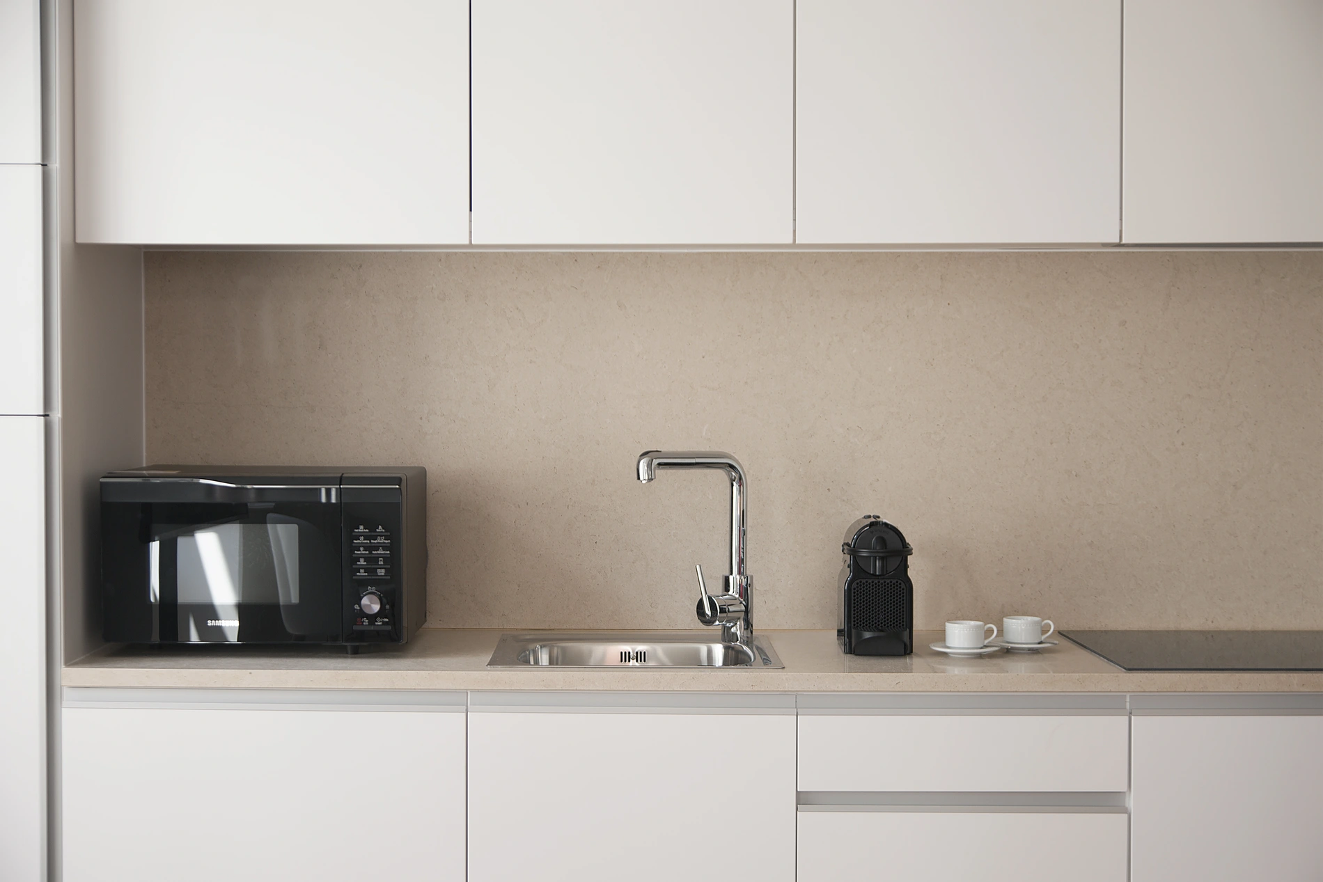 Cozinha moderna com micro-ondas, pia e cafeteira sobre a bancada.