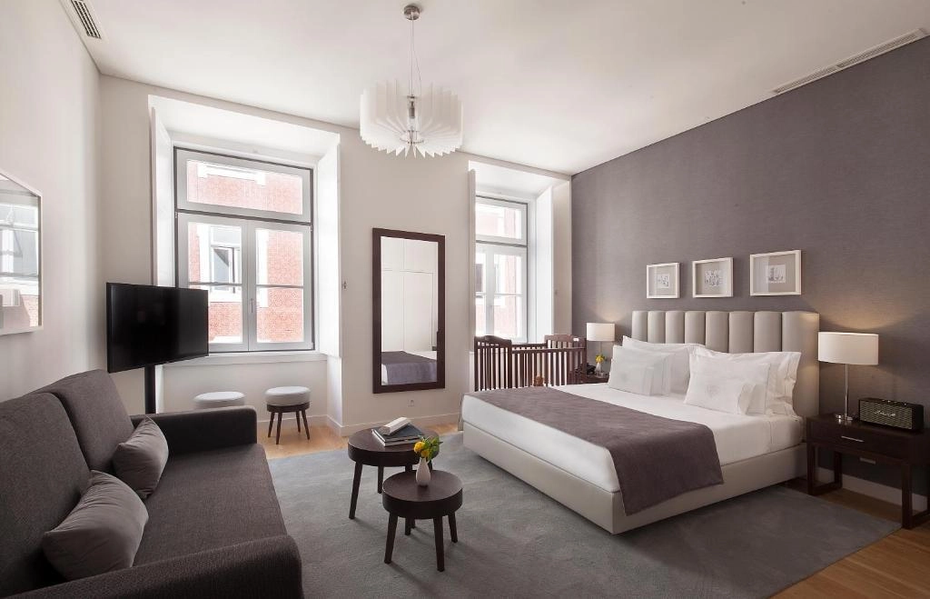 Quarto moderno com cama, sof&aacute;, espelho e janelas grandes.