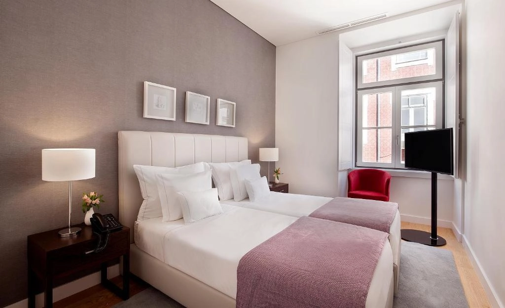 Quarto moderno com cama dupla, poltrona vermelha e lumin&aacute;ria.