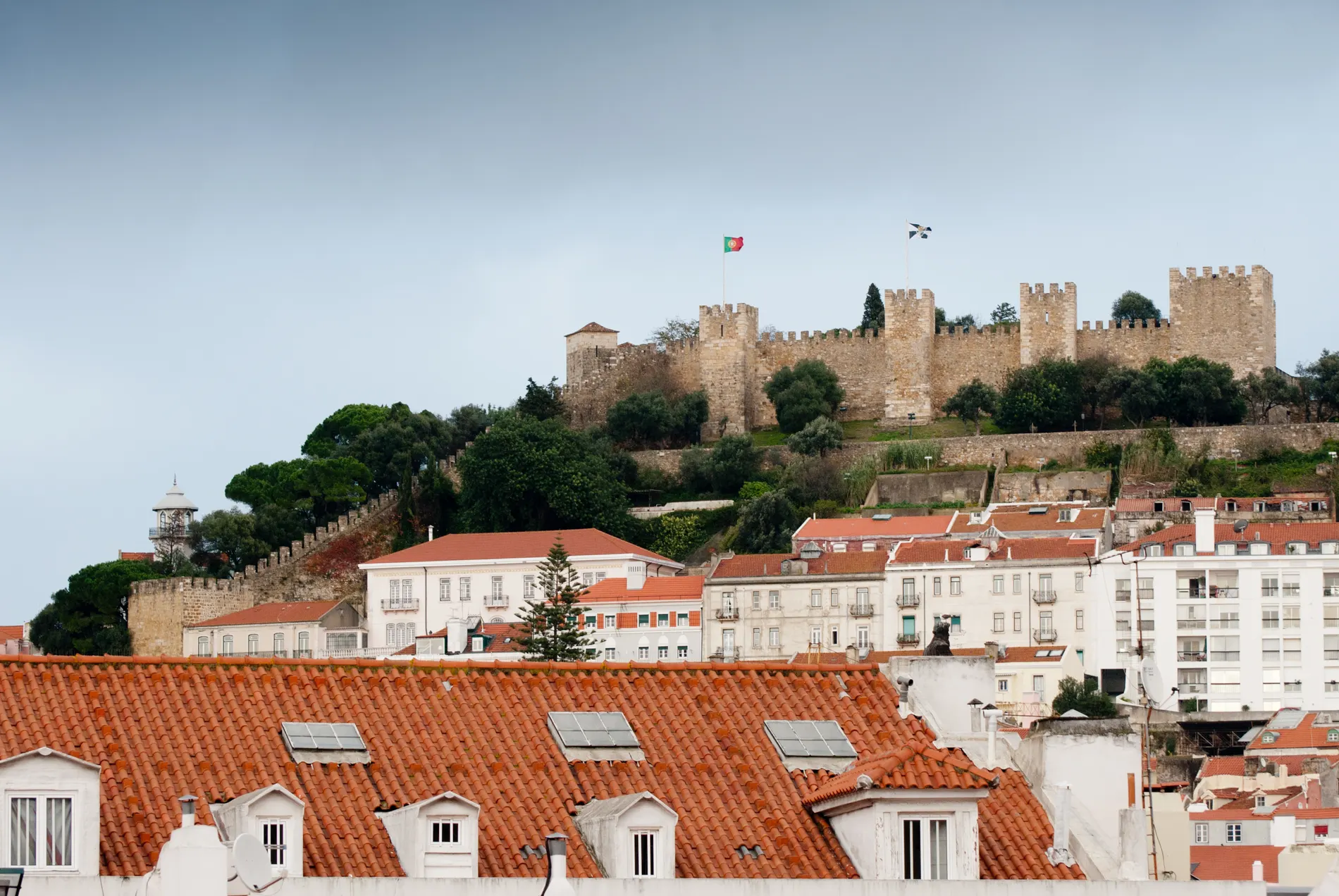 Castelo em colina com bandeira de Portugal sobre telhados vermelhos.