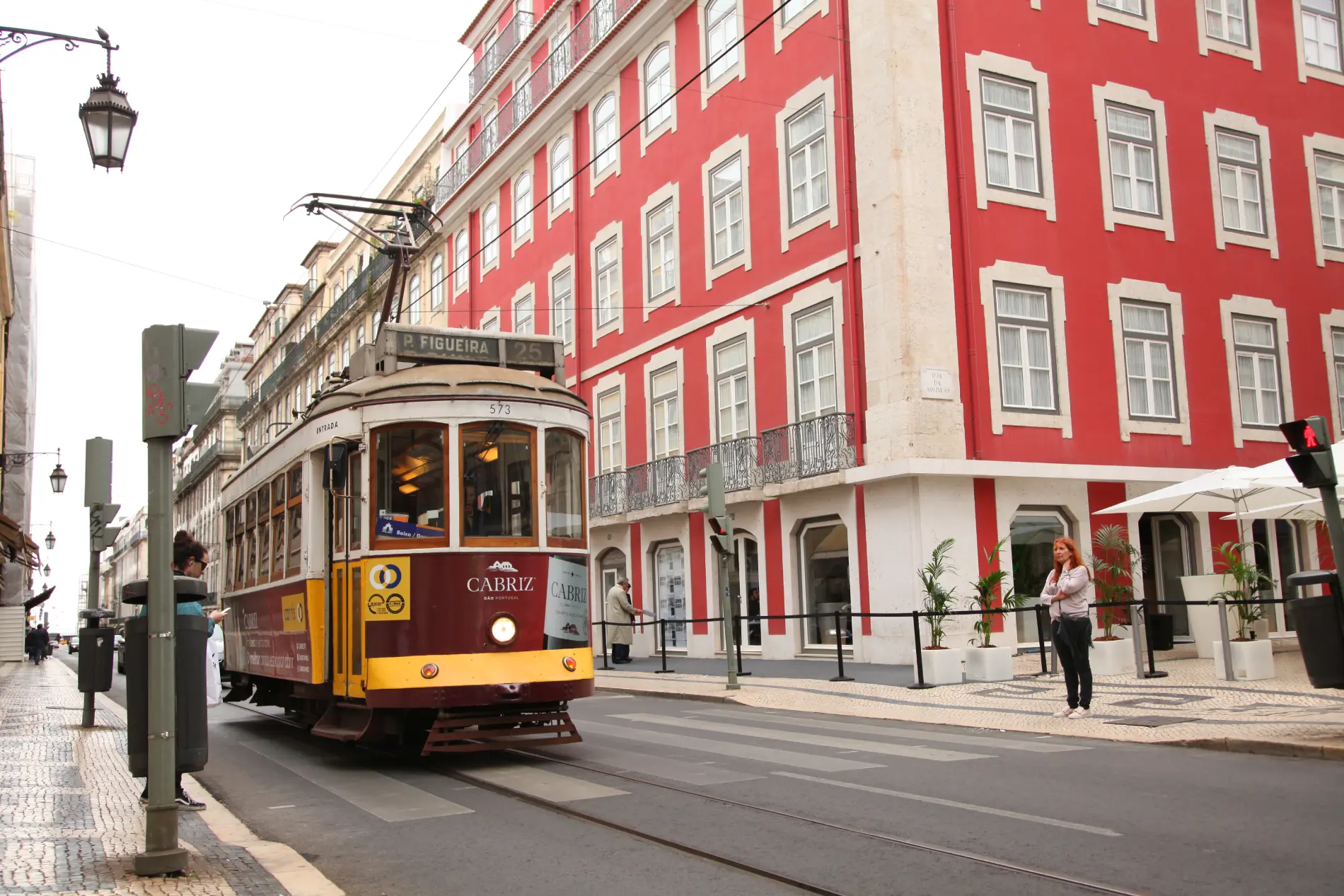 El&eacute;trico em rua com pr&eacute;dio vermelho ao fundo.