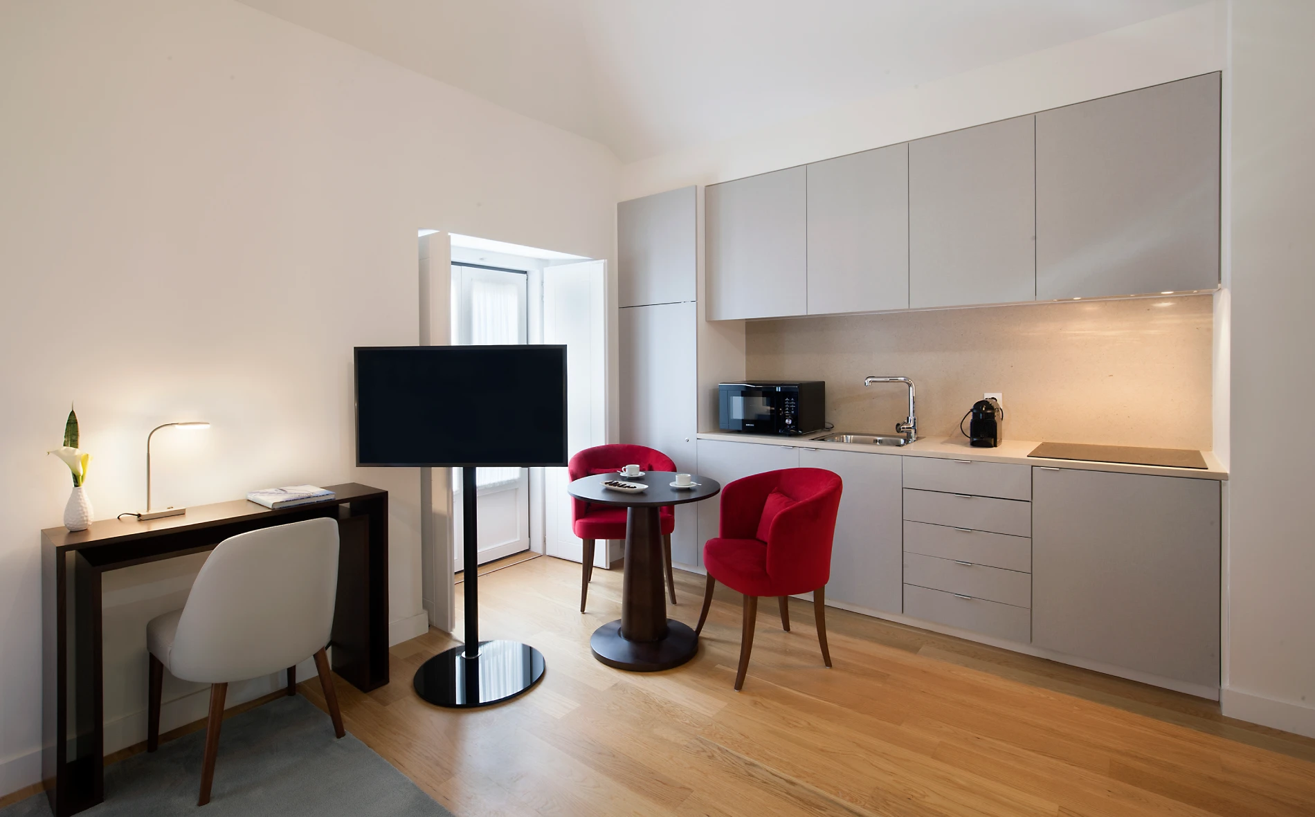 Sala moderna com cozinha compacta e mesa com cadeiras vermelhas.