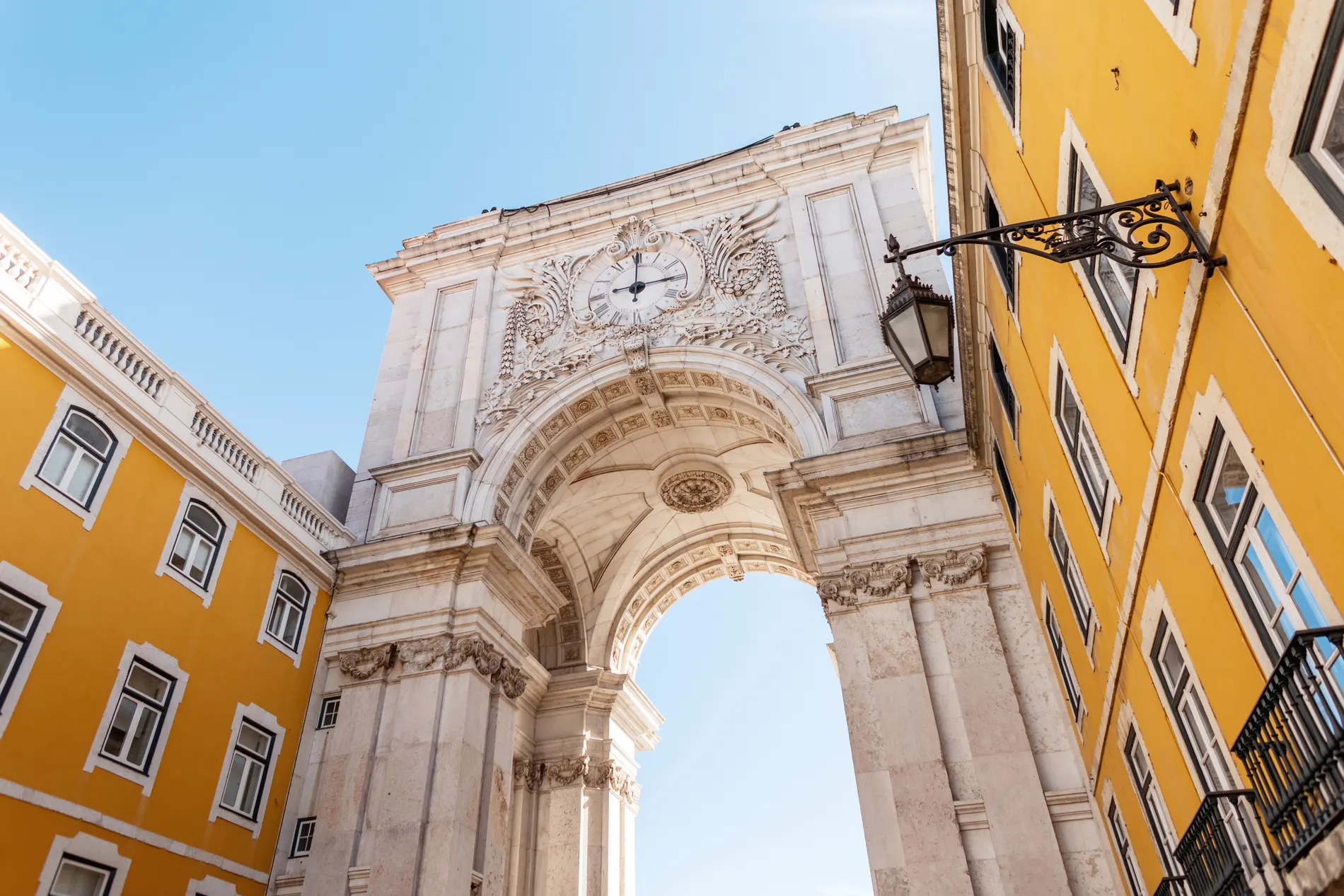 Arco triunfal entre edif&iacute;cios amarelos sob c&eacute;u azul.