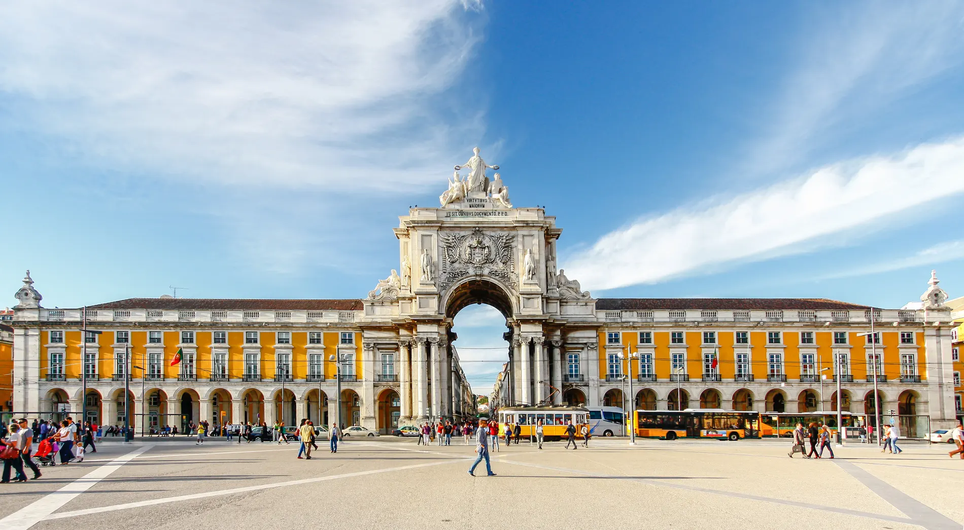Pra&ccedil;a com arco triunfal e edif&iacute;cios amarelos sob c&eacute;u azul.