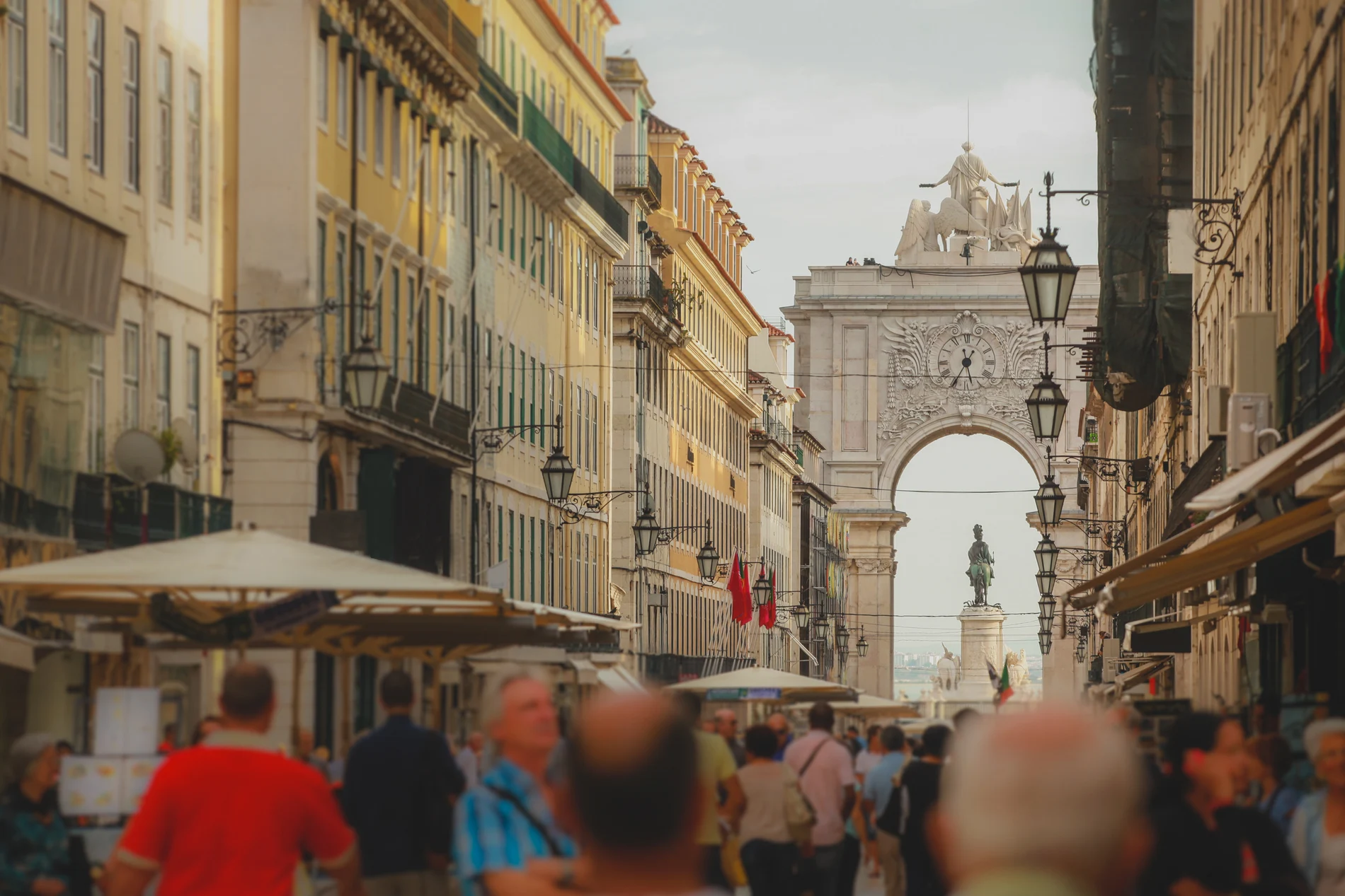 Rua movimentada com arco hist&oacute;rico ao fundo, Lisboa.