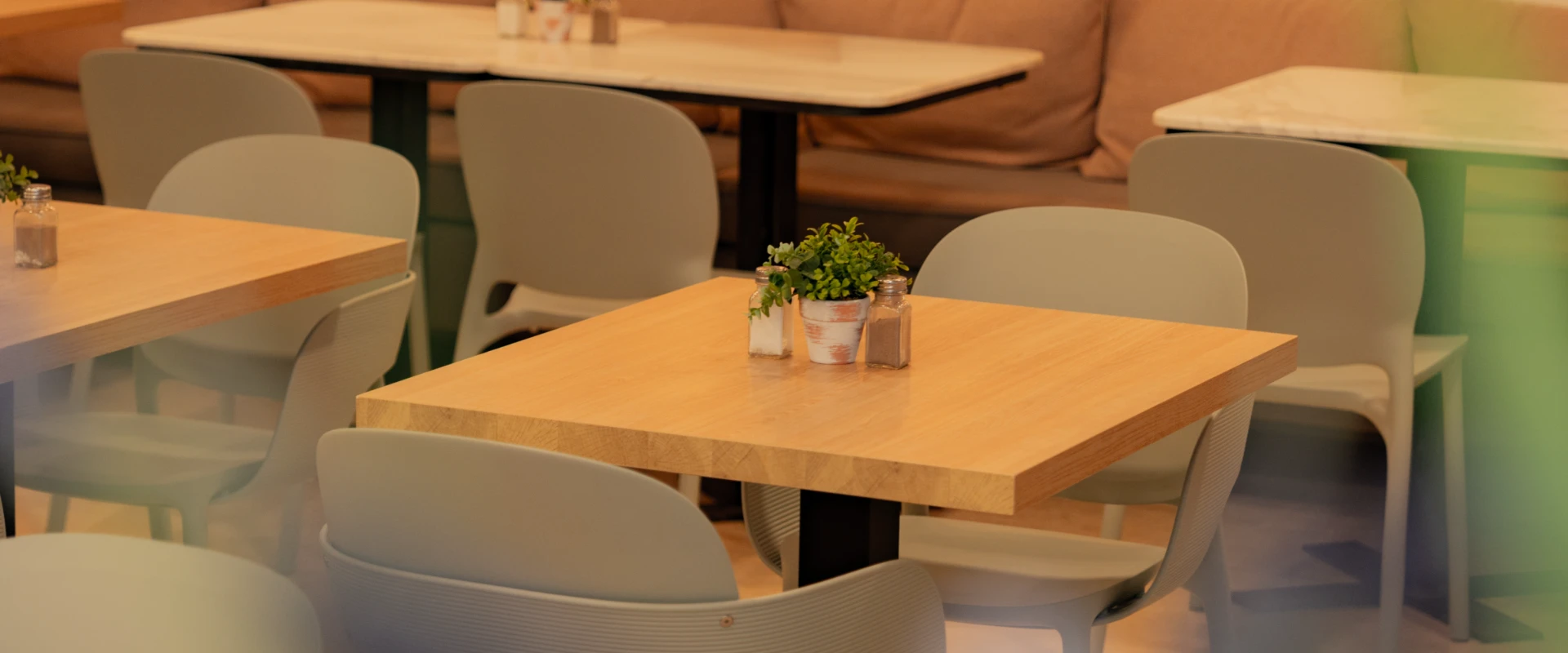 Mesa de restaurante con sillas grises y plantas decorativas al centro.