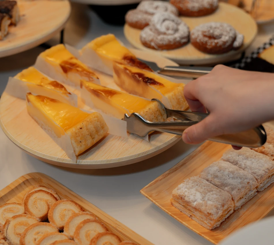 Una mano toma un trozo de pastel de queso con pinzas. Hay varios postres en platos alrededor.