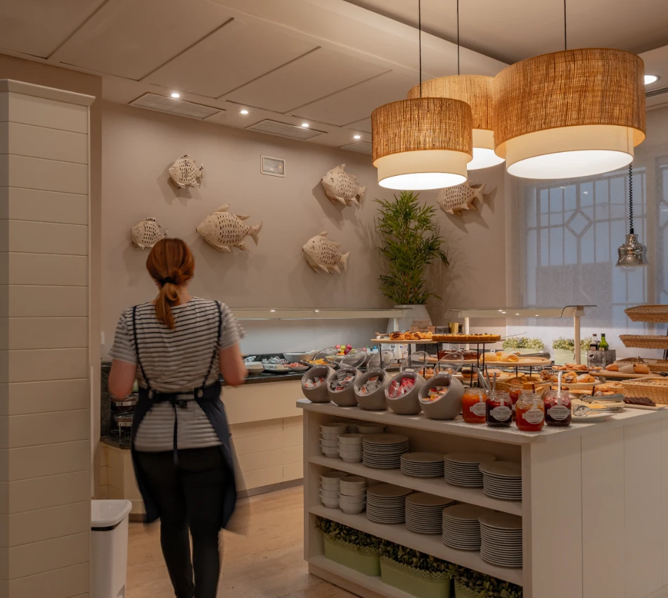 Mujer en buf&eacute; de desayuno, decoraci&oacute;n de peces en la pared y l&aacute;mparas colgantes.