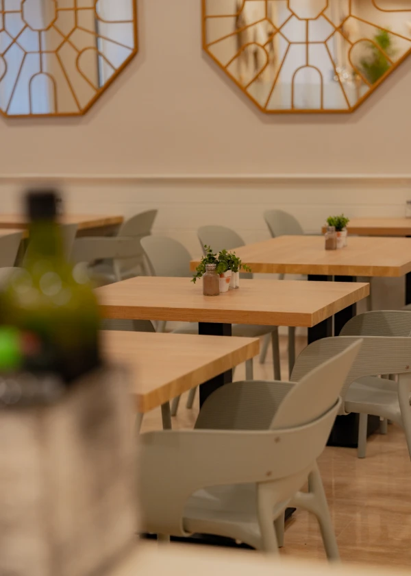 Restaurante con mesas de madera, sillas grises y espejos decorativos en la pared.