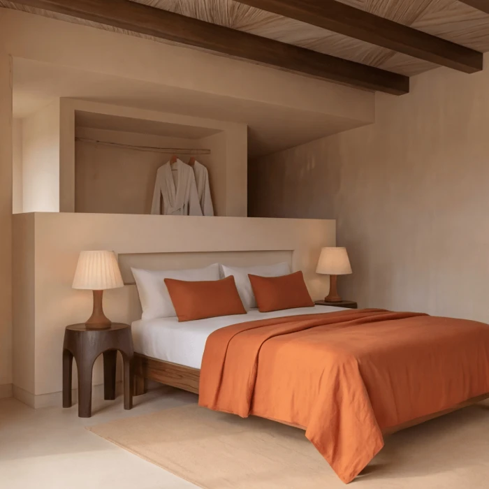 Dormitorio minimalista con cama de s&aacute;banas naranjas y dos l&aacute;mparas sobre mesas de noche.
