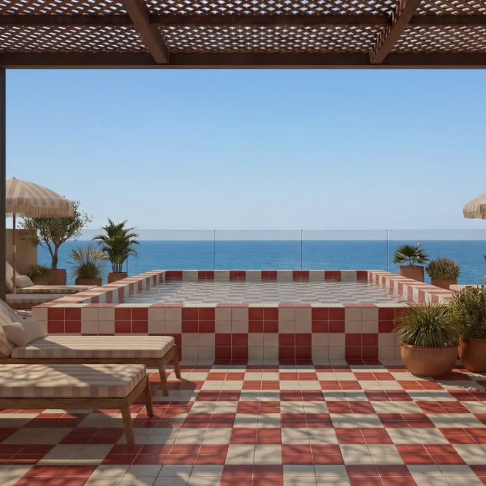 Terraza con piscina de azulejos rojos y blancos, tumbonas y vista al mar azul.