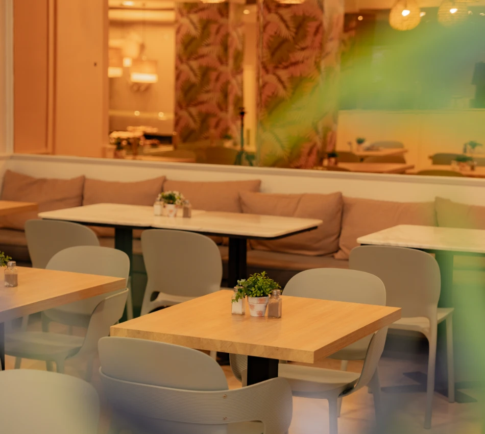Restaurante acogedor con mesas de madera, sillas grises y decoraciones verdes.