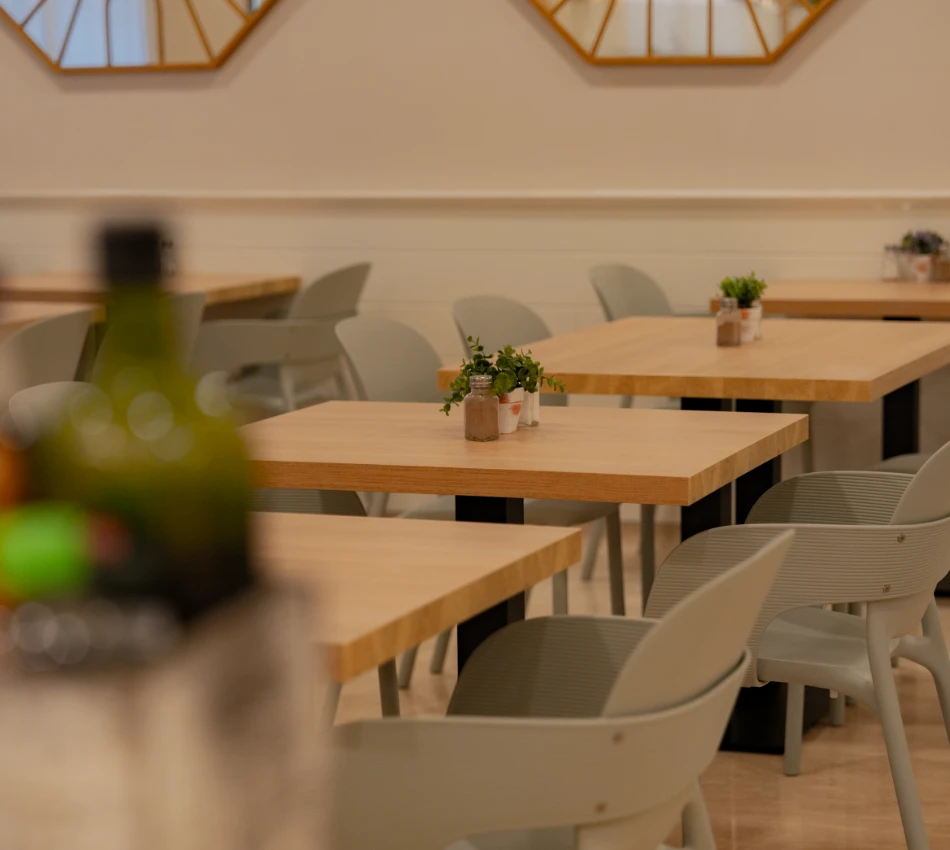 Mesas de madera con sillas grises en un restaurante minimalista; hay plantas como decoraci&oacute;n.