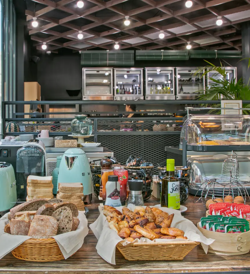 Buffet con panes y bebidas en una cafeter&iacute;a, con vitrinas y luces led.