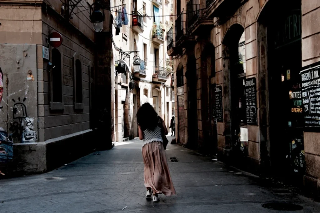 Calle estrecha con una mujer caminando hacia el fondo, edificios antiguos y sombras