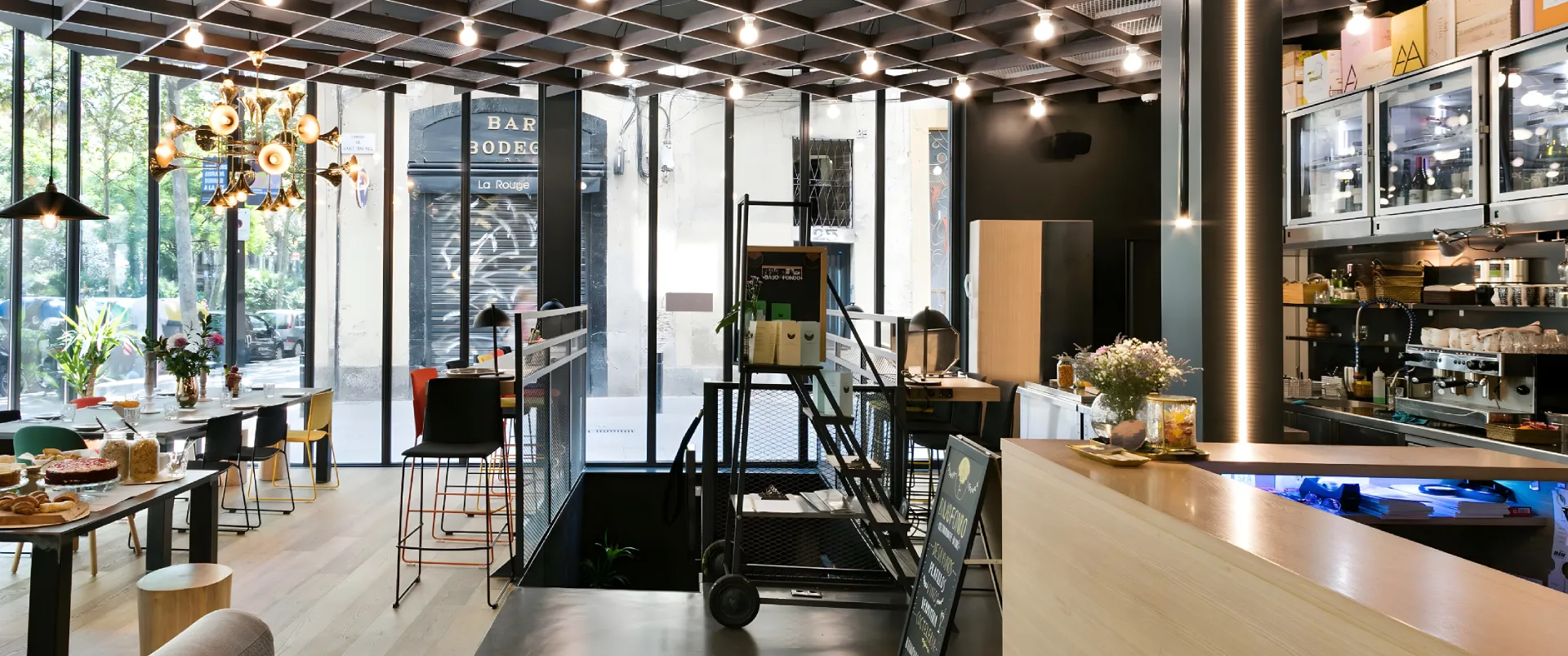 Interior de bar moderno con luces colgantes, mesas y &aacute;rea de cocina/exhibici&oacute;n