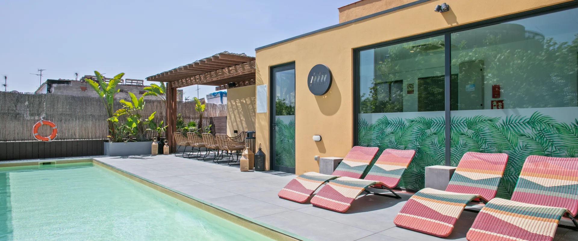 Piscina con tumbonas junto a fachada de hotel y jard&iacute;n con plantas verdes
