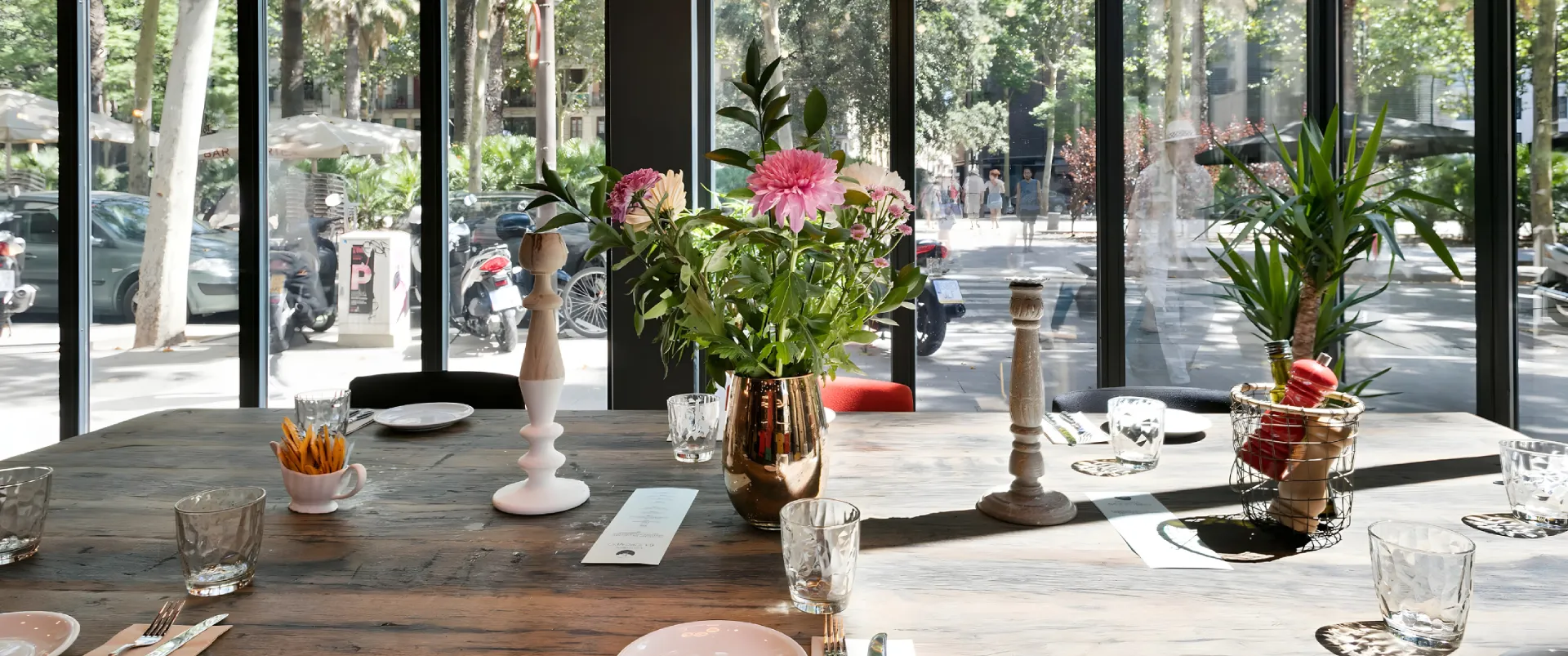 Mesa con flores rosadas en un restaurante junto a ventanales y vista exterior