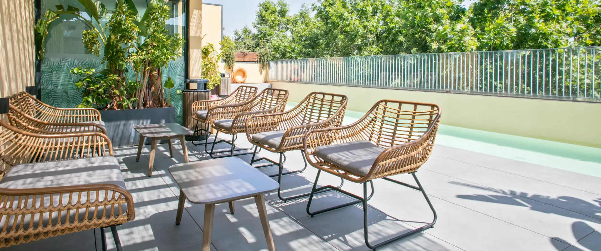 Terraza con sillas y mesa de rat&aacute;n, plantas y luz del sol.