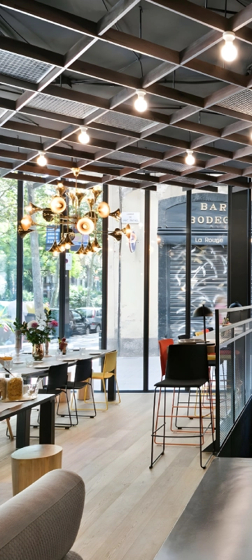 Interior de bar con l&aacute;mparas colgantes y mesas con sillas, luz natural