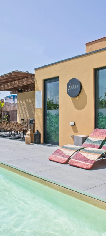 Terraza con piscina y tumbonas, pared beige y puerta azul cielo.