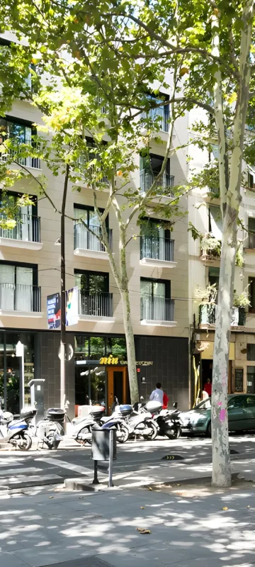 Patio urbano con &aacute;rboles y motos estacionadas frente a edificio de apartamentos.