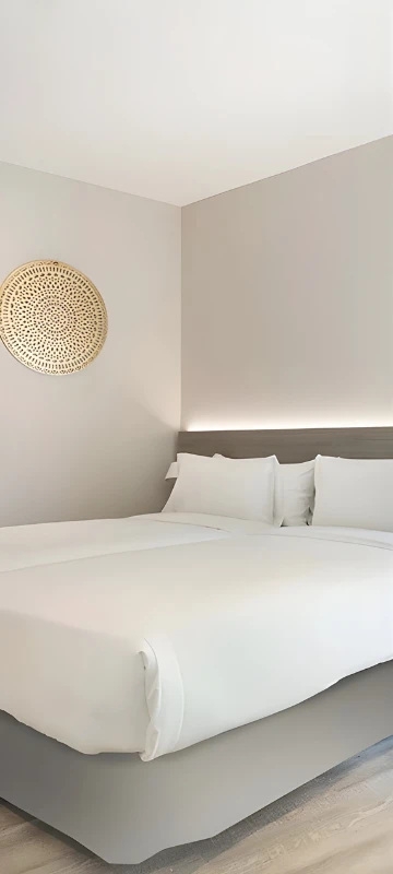 Habitaci&oacute;n minimalista con cama blanca y l&aacute;mpara de pared tejida.