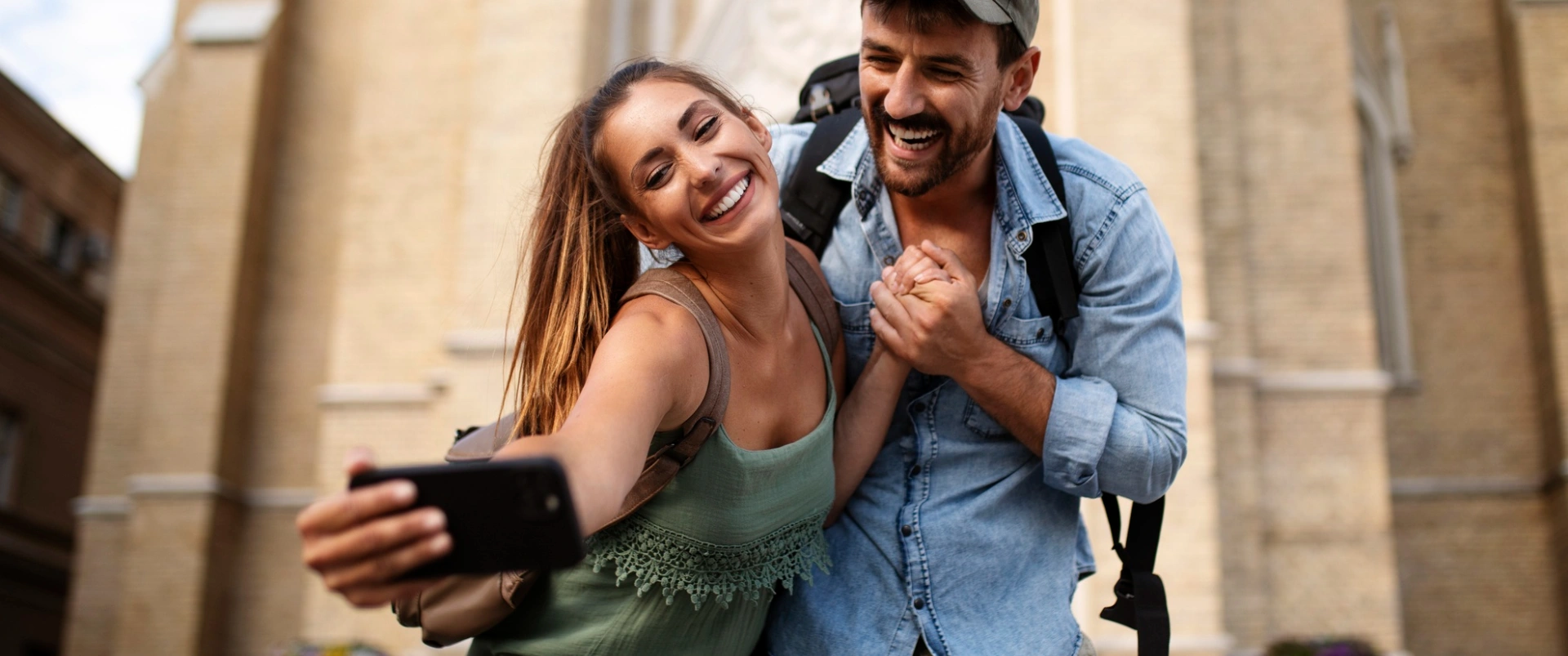 Pareja joven sonriente con mochila, usando el m&oacute;vil en la ciudad.