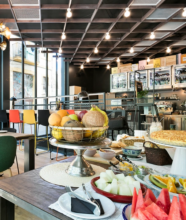 Mesa con frutas y ensaladas en un buffet, l&aacute;mparas y vitrinas al fondo.