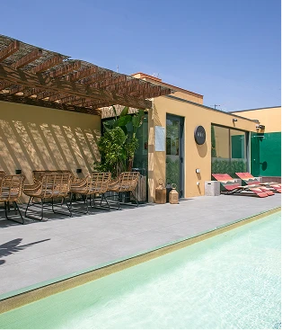 Patio con piscina y sillones junto a una casa amarilla y una pared verde