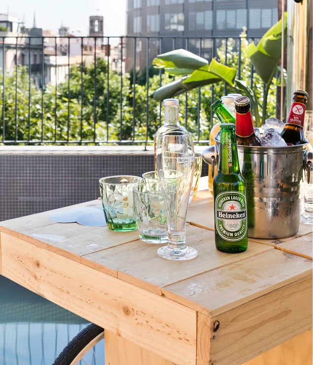Mesa con botellas y vasos sobre terraza, ciudad al fondo.