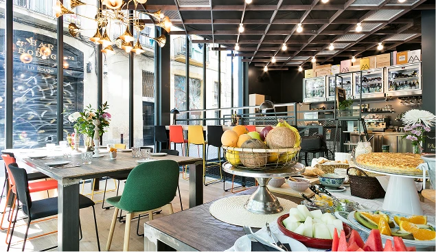 Interior de cafetería con mesas, frutas y lámparas colgantes.