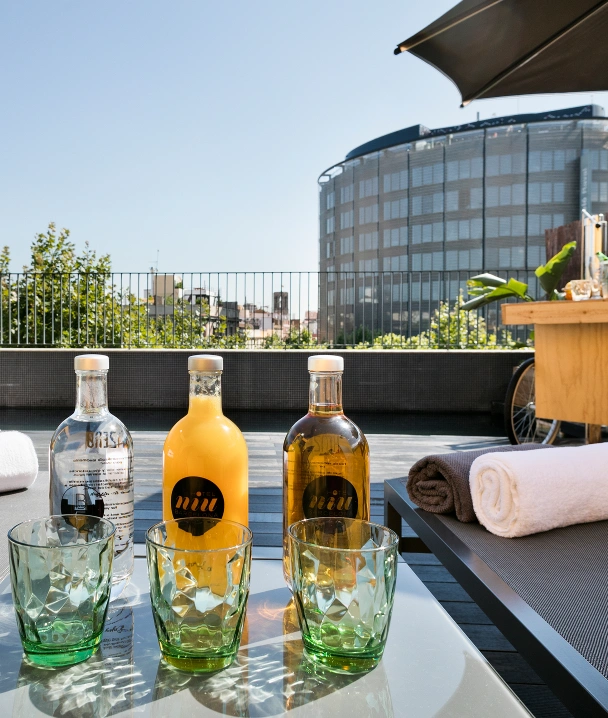 Botellas y vasos con bebidas en una terraza con sombrilla y edificio al fondo