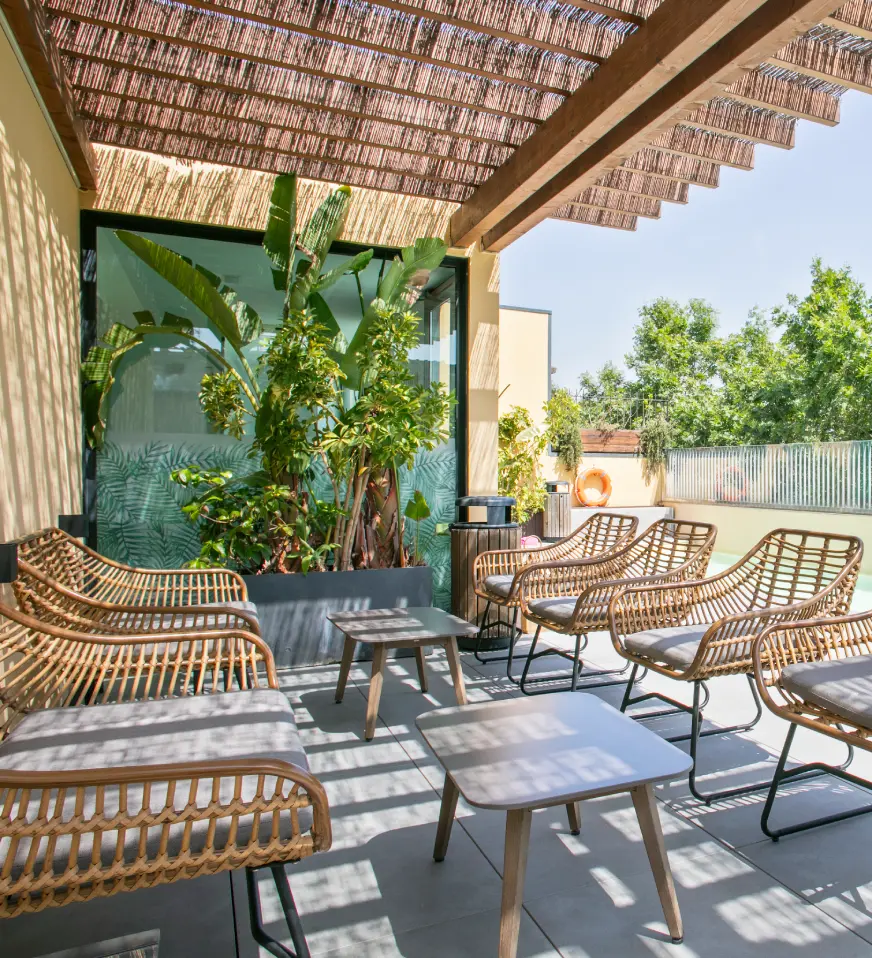 Terraza con muebles de mimbre, plantas y techo de madera con hojas de bamb&uacute;.