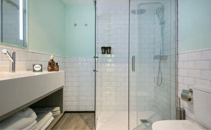 Ba&ntilde;o moderno con ducha de vidrio, lavabo y accesorios en tonos claros.