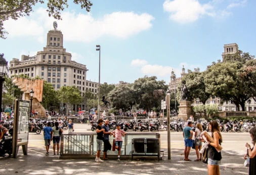 Vista de plaza urbana con edificios, &aacute;rboles y personas caminando