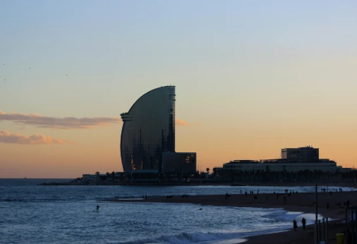 Atardecer junto a un gran edificio circular junto al mar y la playa.