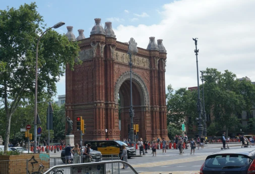 Arco monumental de ladrillo rojo en una avenida con &aacute;rboles y tr&aacute;fico