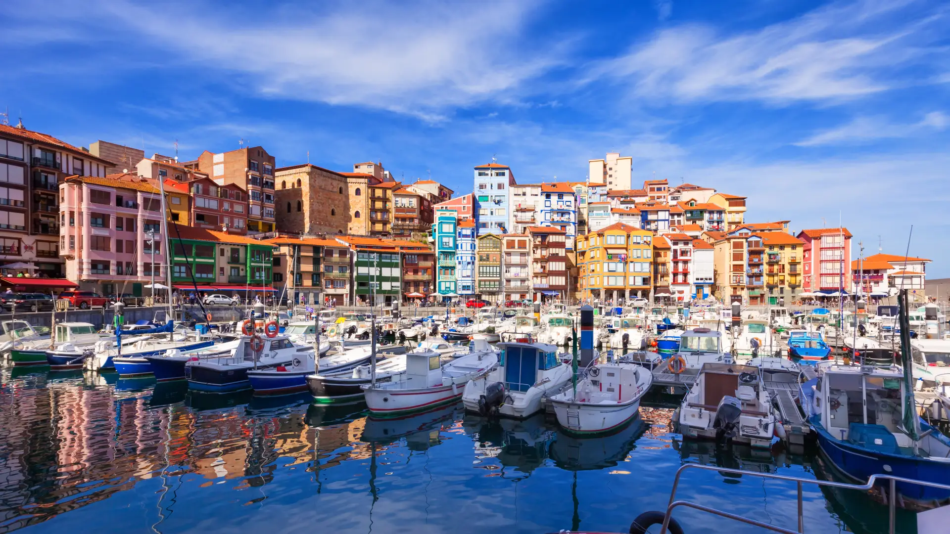 Puerto con barcos y edificios de colores bajo cielo azul con nubes