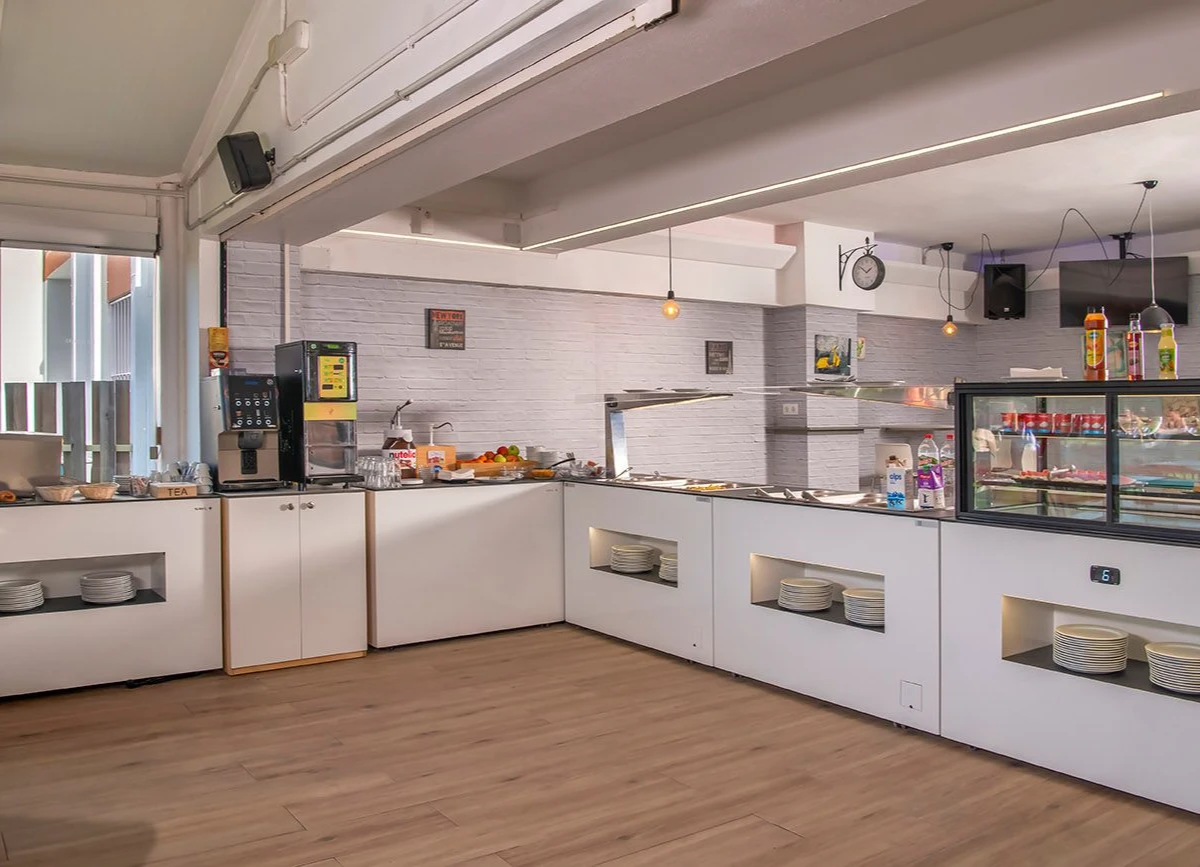 Cafetería con barra blanca, máquina de café, buffet y fregadero en cocina.