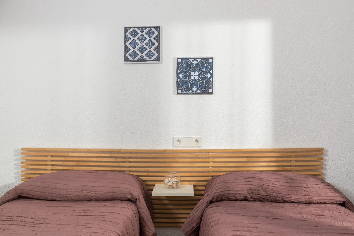 Habitación con dos camas y panel de madera, pared con cuadros azules.