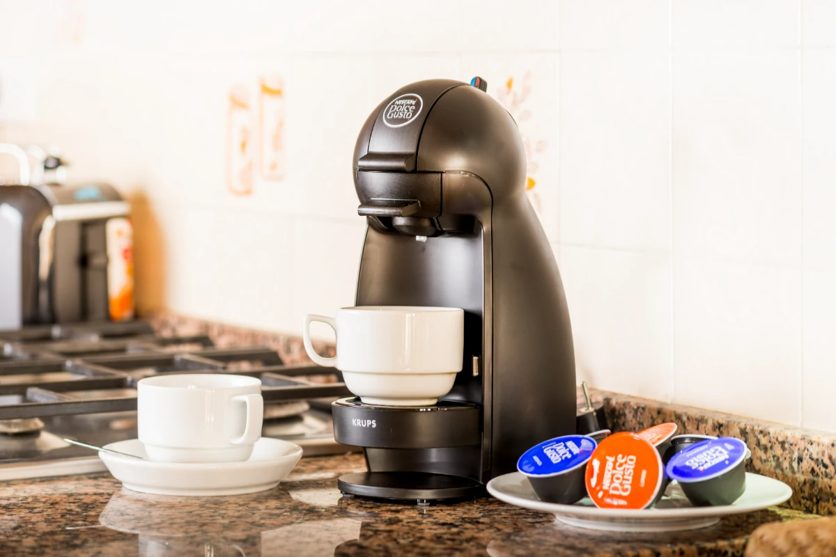 Cafetera Nescafé Dolce Gusto con tazas y cápsulas en encimera de cocina