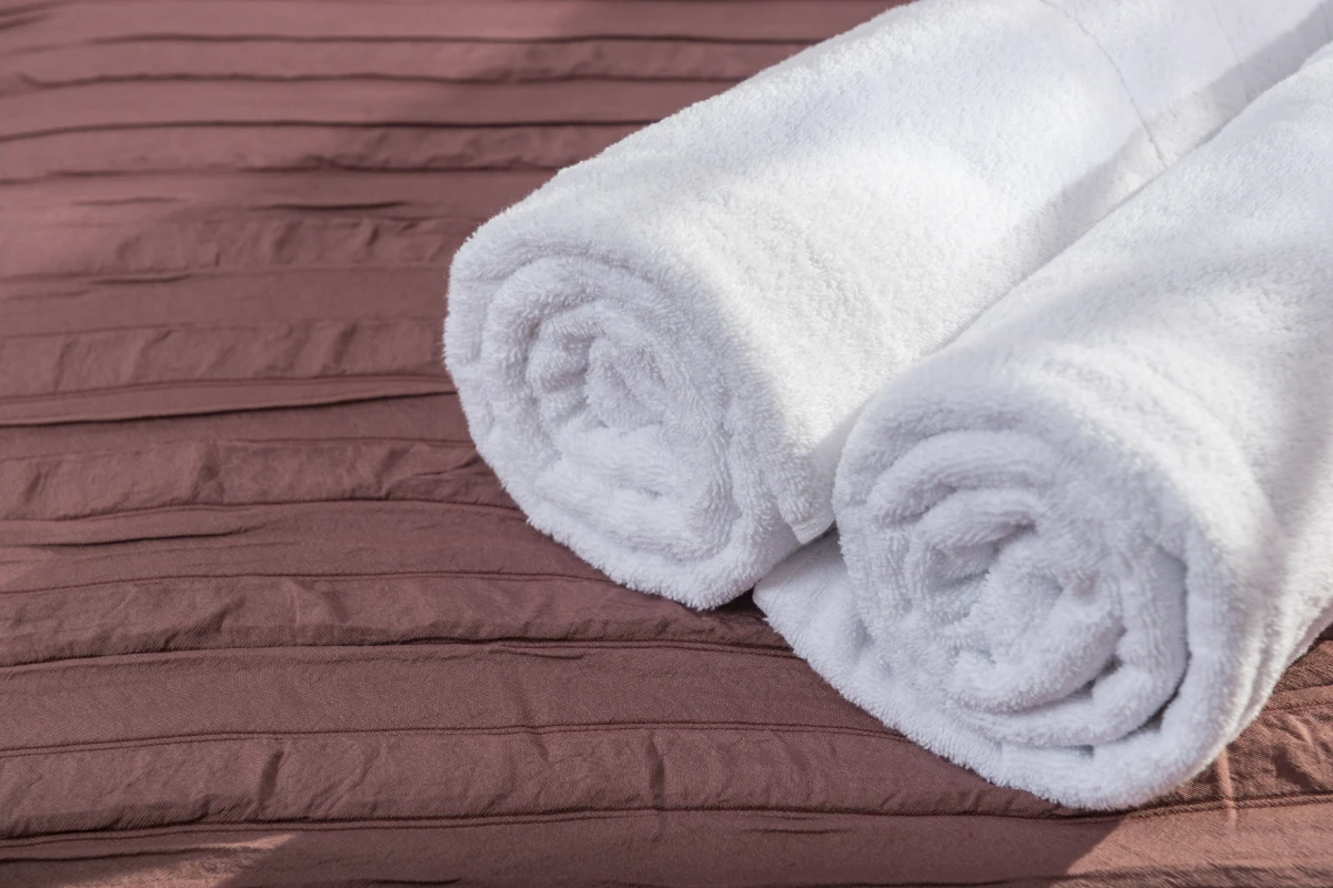 Toallas blancas enrolladas sobre cama marrón con fondo de madera