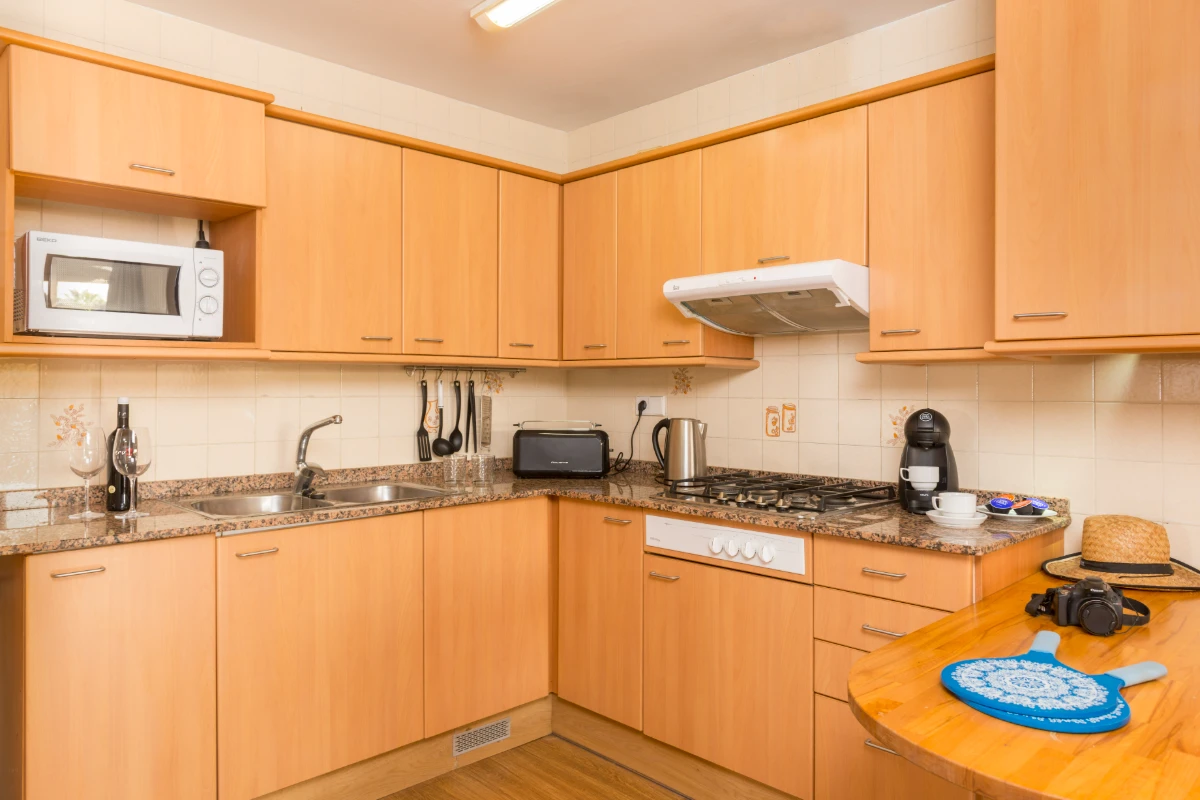 Cocina luminosa con muebles de madera, encimera y electrodomésticos.