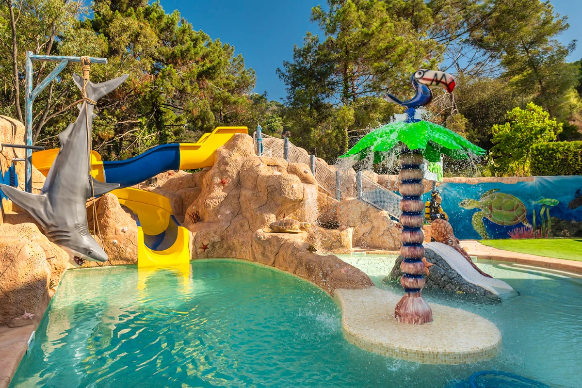 Parque acuático con toboganes y surtidor con delfín, agua verde y azul