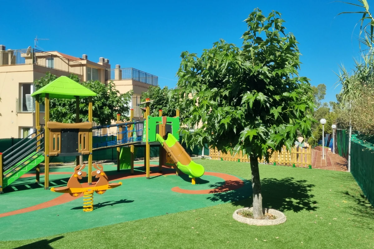 Parque infantil con tobogán verde y área de juegos al aire libre, cielo azul