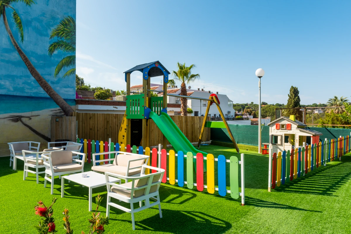 Parque infantil con tobogán y valla multicolor en jardín verde soleado