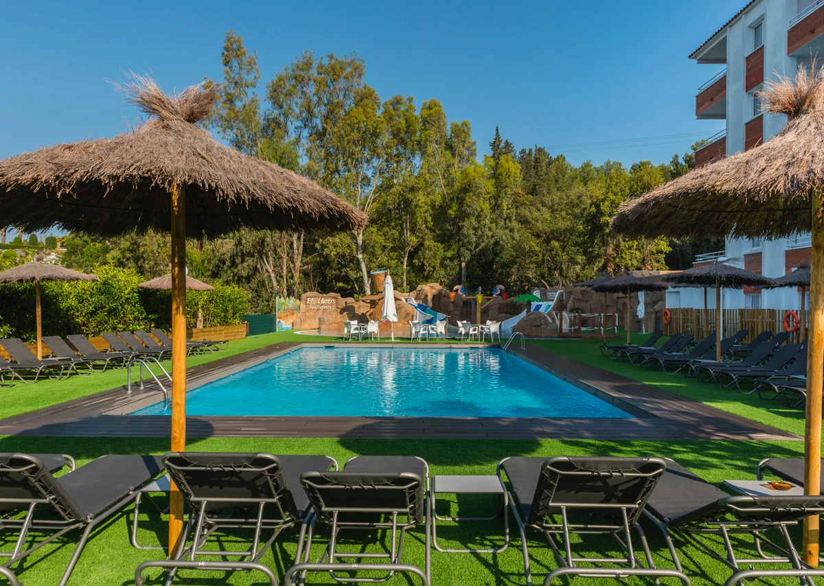Piscina y tumbonas en un resort con techo de paja y jardín al sol